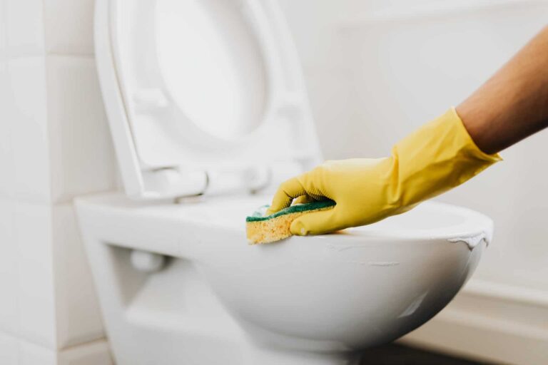 a yellow rubber gloved hand is scrubbing a white toilet with a sponge