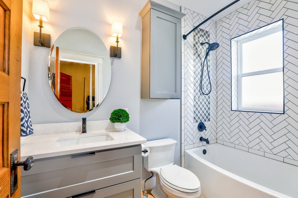 Elegant modern bathroom featuring chevron tiles, oval mirror, and sleek fixtures for a contemporary look.