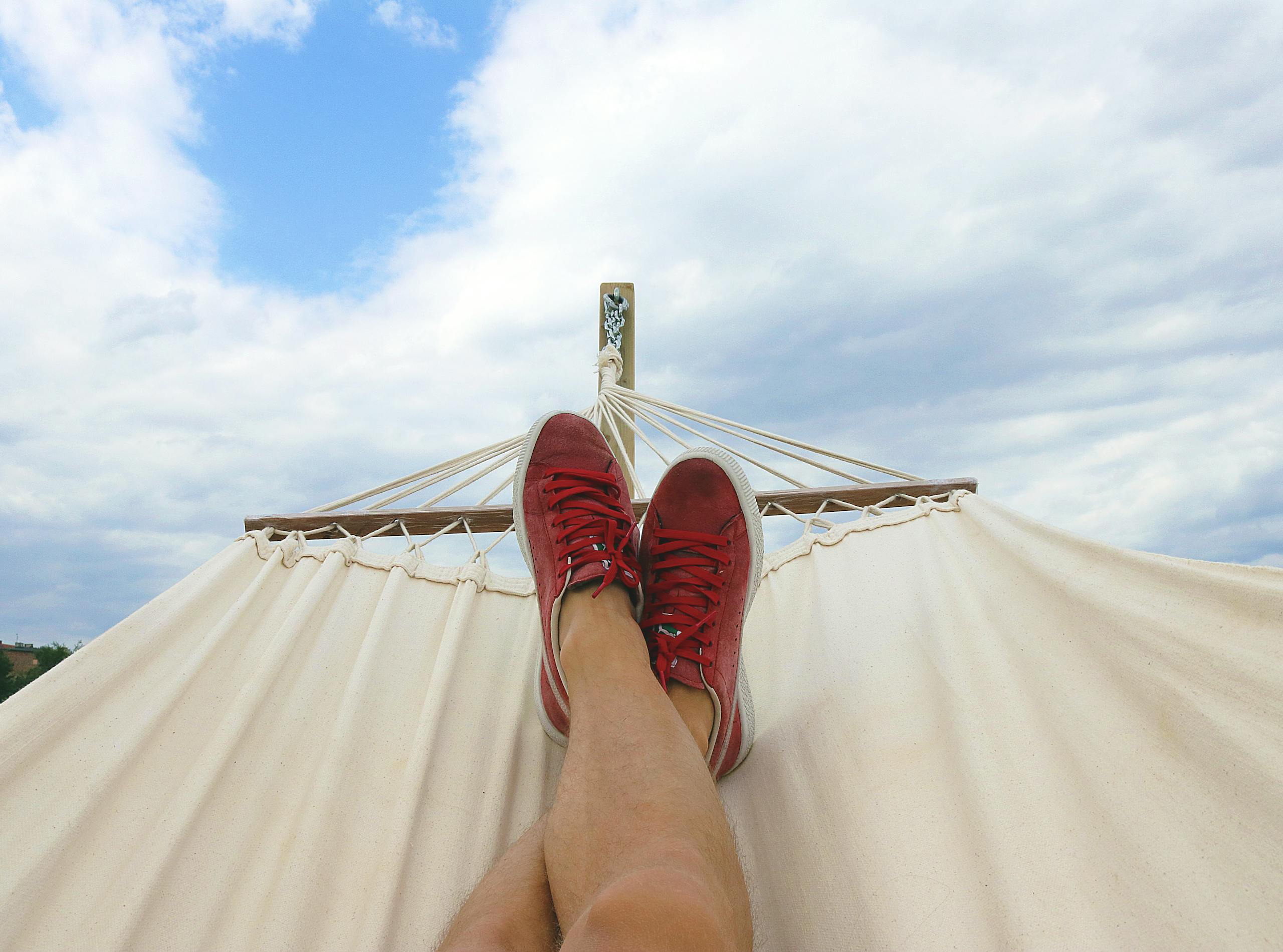 Feet resting on a hammock with red sneakers, epitomizing summer relaxation and leisure outdoors.