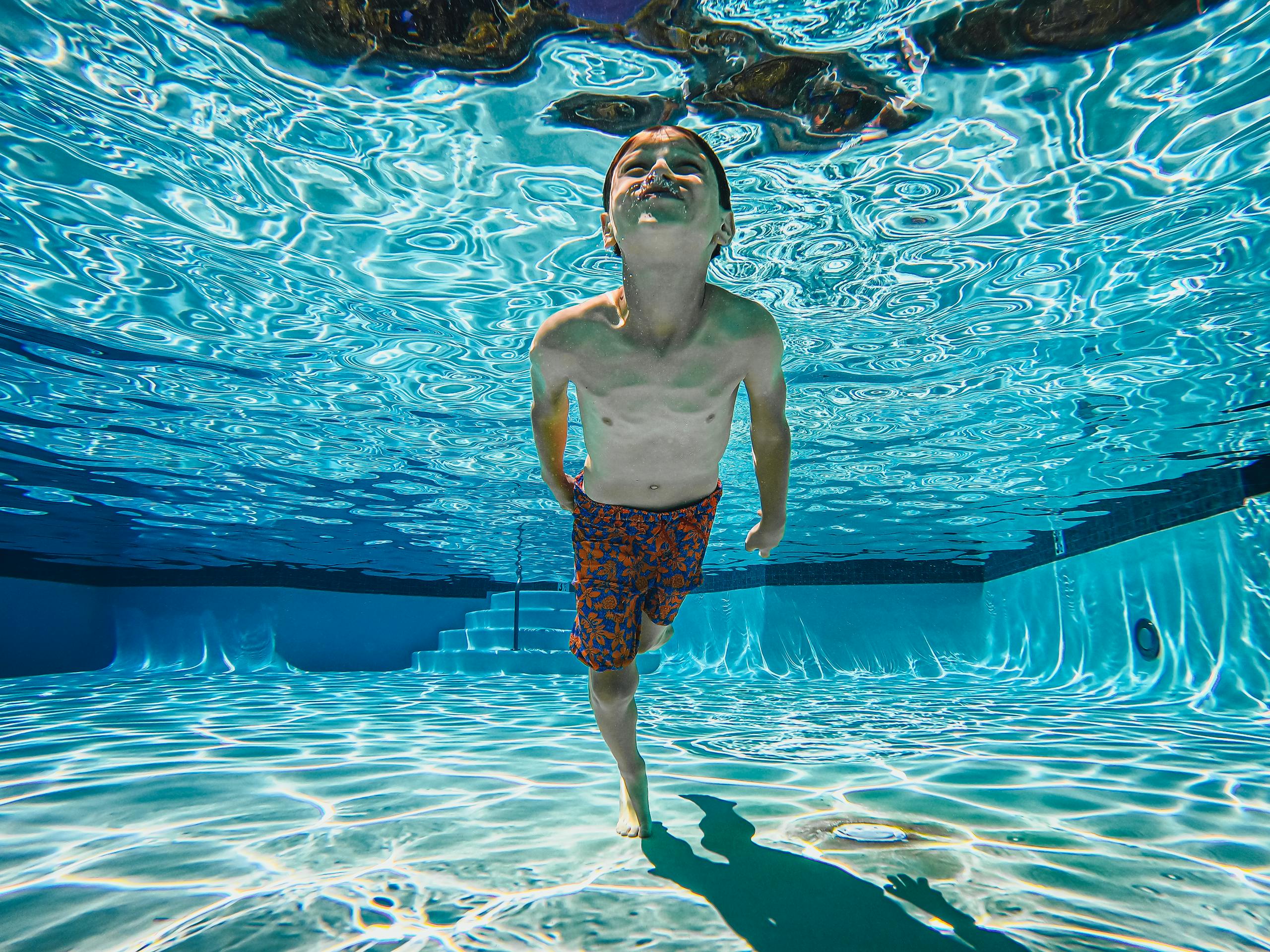 A joyful child swims underwater in a sunlit swimming pool, showcasing fun and skill.