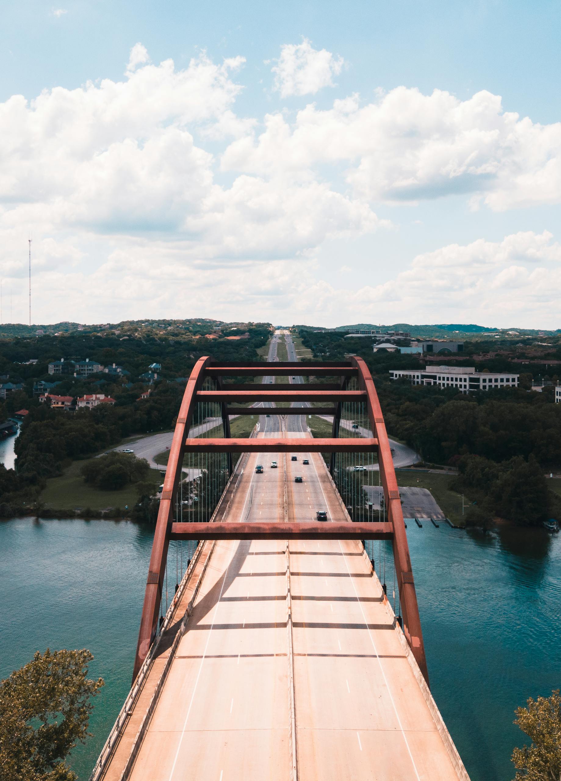 A stunning aerial shot of the iconic Pennybacker Bridge in Austin over the Colorado River on a sunny day.