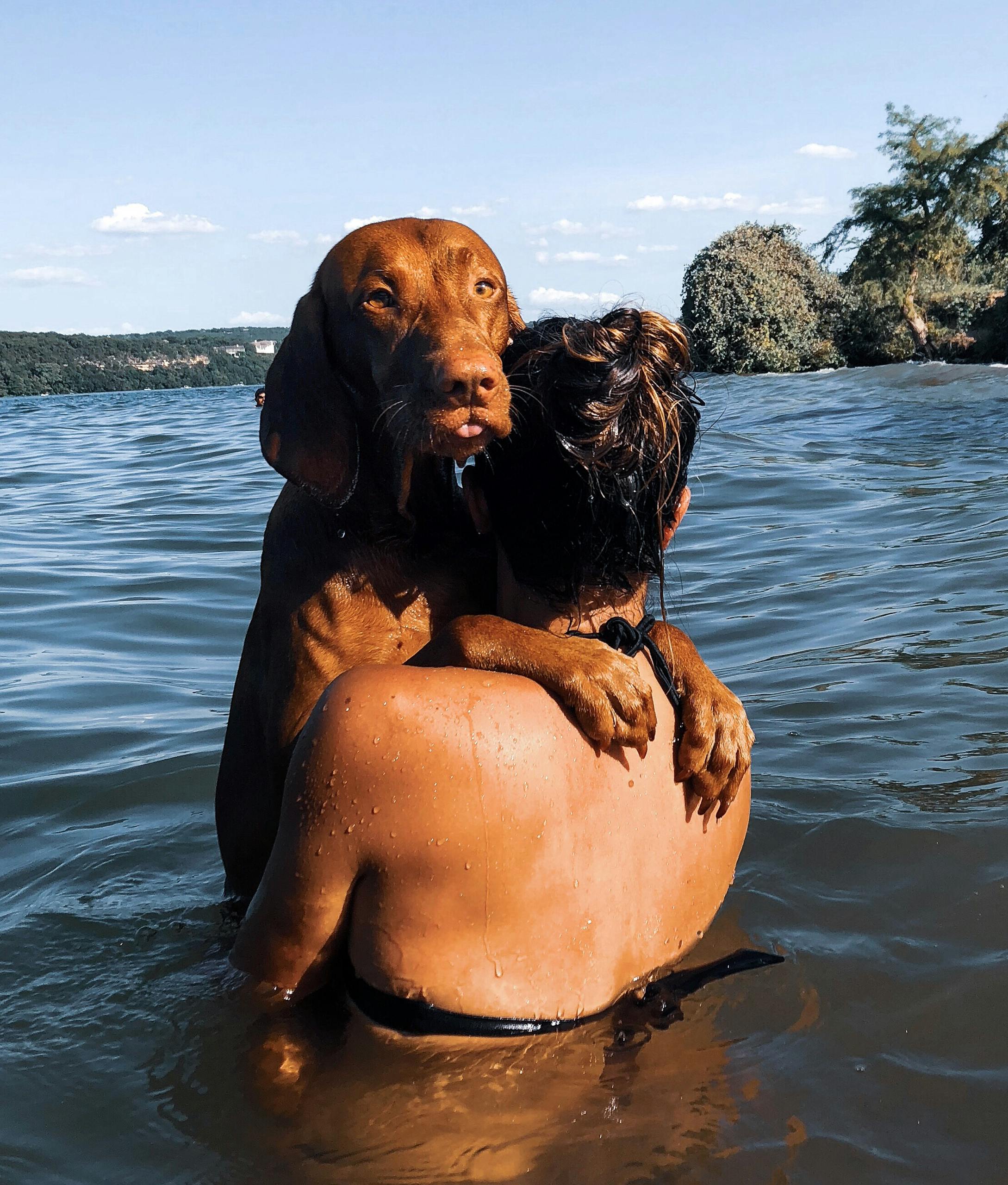 A woman embraces her dog in the lake, enjoying a summer day at Austin, TX.