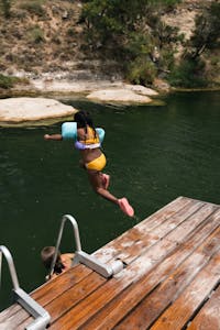 A young girl joyfully jumps into a river from a wooden dock during a sunny summer day in Austin, Texas.