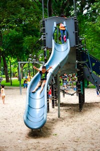 Children having fun on a slide in a lively park playground on a bright day.