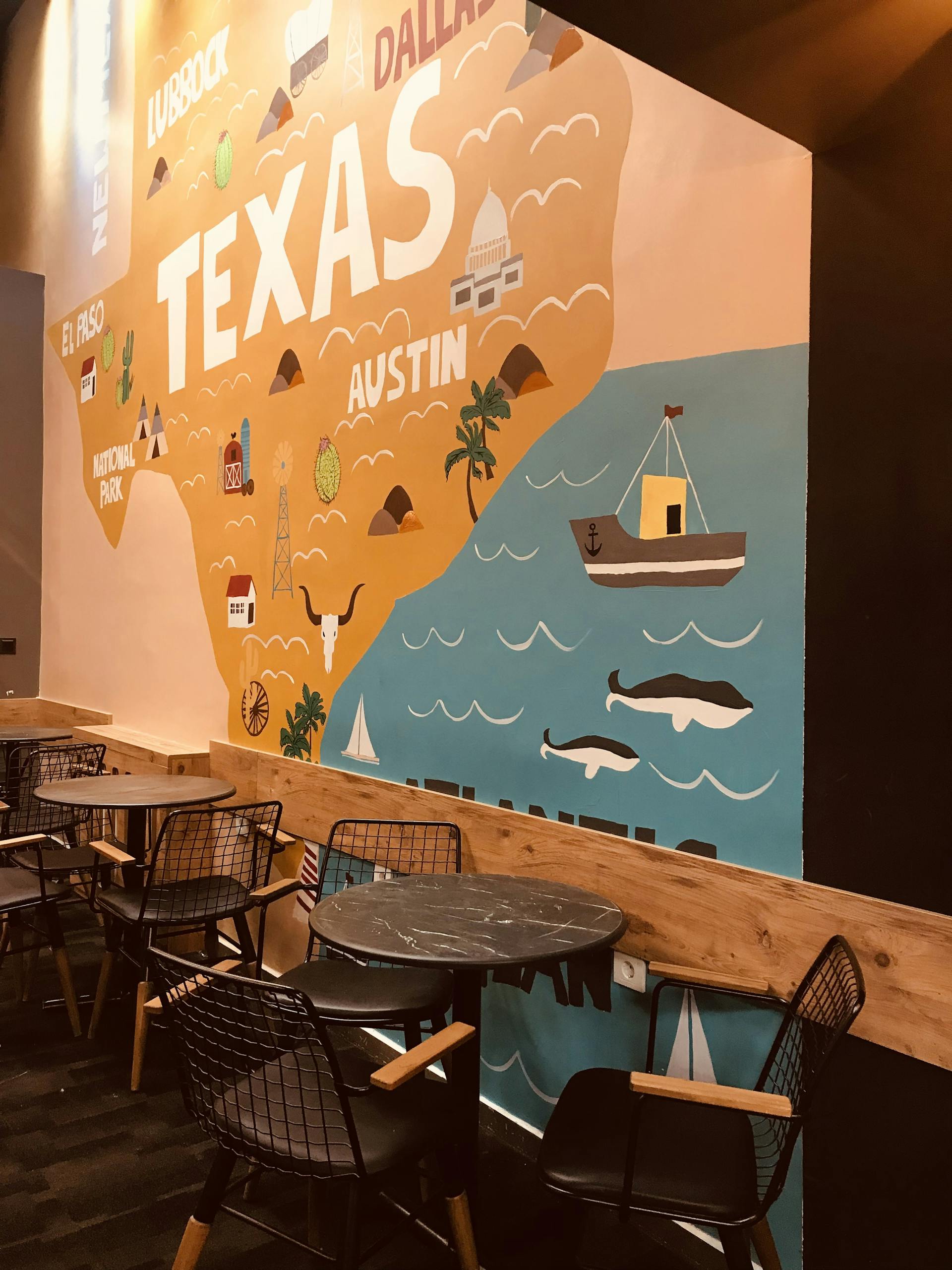 Vibrant Texas-themed wall mural with seating area in modern cafe. Artistic and inviting ambiance.